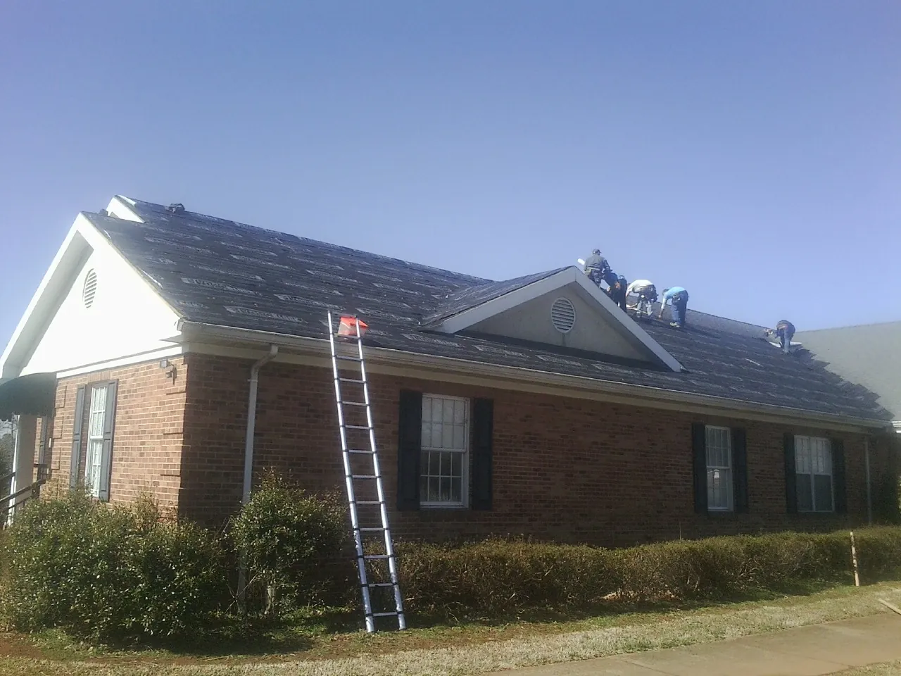 Crew tearing shingles off a brick ranch roof with a ladder set — Metal Roof Repair work by our crew in Indian Valley