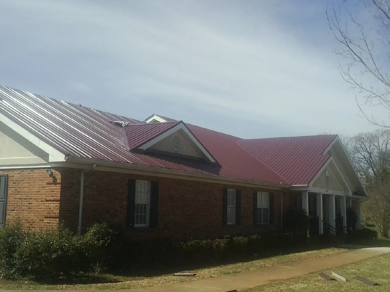 Red metal roof with gabled entries on a long brick building, from a Hail Damage Roof Repair job in Indian Valley